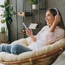 woman lounging in an armchair, listening to music using phone and headphones