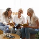 three mature women discussing a book during a book club session in a home setting