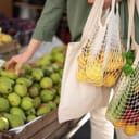 A woman choosing fruit at a farmers market and placing them in reusable bags