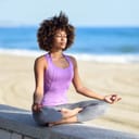 A young woman meditating on a stone wall next to a beach