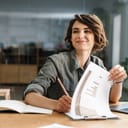Close-up of a smiling woman, joyfully taking notes while seated at an office table.