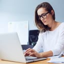 focused young businesswoman working on a laptop in a well-lit, contemporary office