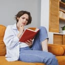 A puzzled young woman reading a book while sitting on a couch