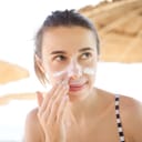 Girl applying sunscreen to her face at the beach