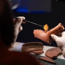 over-the-shoulder view of an archeologist carefully cleaning an ancient vessel in the office during a late-night work session