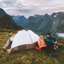 A couple talking with a tent behind them, camping outdoors as they explore the mountains of Norway.