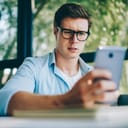 young man with glasses looking at his smartphone with uncertainty, reading an article