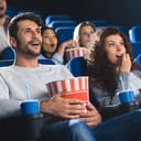 emotional couple with popcorn watching movie together in cinema
