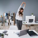 A young businesswoman takes a break at her desk to stretch her arms.