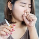 A woman holding a cigarette caughing