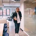 young man in a casual attire and glasses holding a laptop while walking by a glass wall in a spacious modern office, leaving for a lunch break