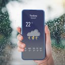 Woman checking the weather forecast on her smartphone, displaying current conditions.