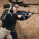 young woman practicing rifle shooting with an AR15 under the guidance of a male instructor at a shooting range