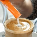 Close-up with selective focus pouring sugar to a latte.