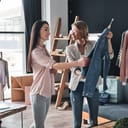 A clothing store employee showing a denim jacket to a customer