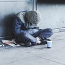 Homeless man sitting on the street in the shadow of the building and begging for help and money. Problems of big modern cities.