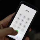 Hand holding cell phone with emergency number 911 on black background