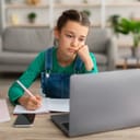 Bored young girl looking at laptop while taking notes