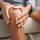 close-up of a man holding his knee with both hands, representing osteoarthritis pain