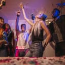 Young men and women having fun at a colorful house party. Friends dancing in joy holding drinks at a house party.