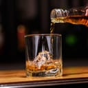 Pouring whiskey into a glass with ice cubes from a bottle