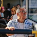 Close-up of an elderly man sitting in a bus and looking out the window.