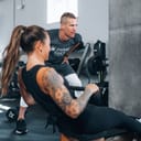 Woman at gym on a rowing machine alongside her personal trainer