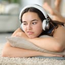 Disappointed woman listening to music with headphone lying on a carpet at home