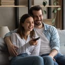 A smiling couple sitting on a couch watching TV