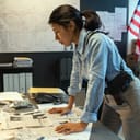 A = police detective leaning on a table covered with paper evidence