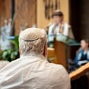 elderly man with white hair in a prayer shawl and yarmulke in a synagogue
