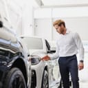 young man dressed formally inspecting a car at a vehicle dealership store