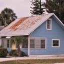 blue costal house with a corroded metal roof and jalousie windows