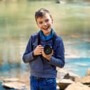 Young boy holds a camera while standing in front of a river