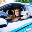 Young woman smiling and showing her new driving license thought the car window
