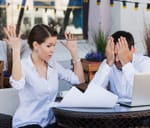 A woman throwing her hands up in the air while a man covers his face with hands in disapproving fashion