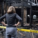 woman looks at a burned down house