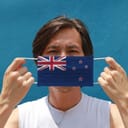 Man holding a face mask up to his face that is designed to look like the New Zealand flag