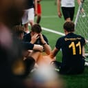 Soccer players, looking visibly upset, sit on the ground after losing a match.
