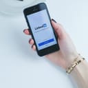 Close-up of hand holding a phone showing the Linkedin app.
