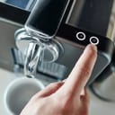 Close-up photo of someone pressing a button on the top of a coffee machine