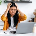 stressed woman at a laptop with her hands on her head in distress