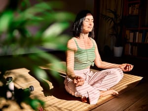 A woman practicing meditation in her room during a sunny day