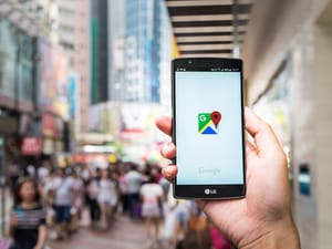 A person on busy city street holding a phone with Google Maps app opened