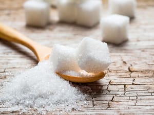 A wooden spoon with granulated and cubed sugar