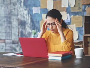 An upset woman sitting at a table looking at a laptop