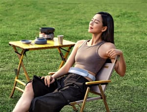 A woman sitting on a lawn chair wearing her portable air conditioner around her waist