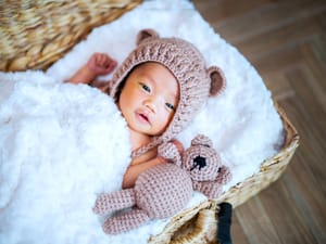 A newborn baby in a whicker basket with a stuffed bear and smiling