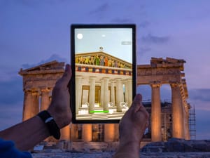 A man holds up a tablet showing a digitally overlayed virtual reconstruction of the ancient Parthenon temple, at the Acropolis Hill in Athens, Greece
