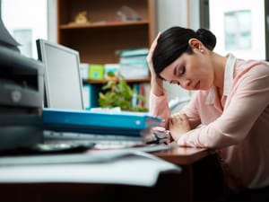 Tired woman sitting at a table at work surrounded by a pile of documents